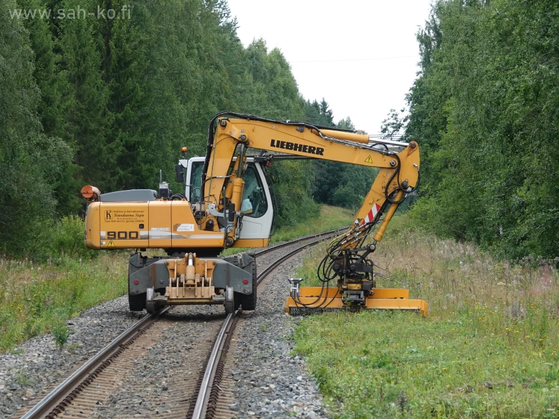 Raiko-vesakonraivain, työkoneena kaivinkone junaratavarustuksella lyhentää kasvustoa junaradan reunoilta.